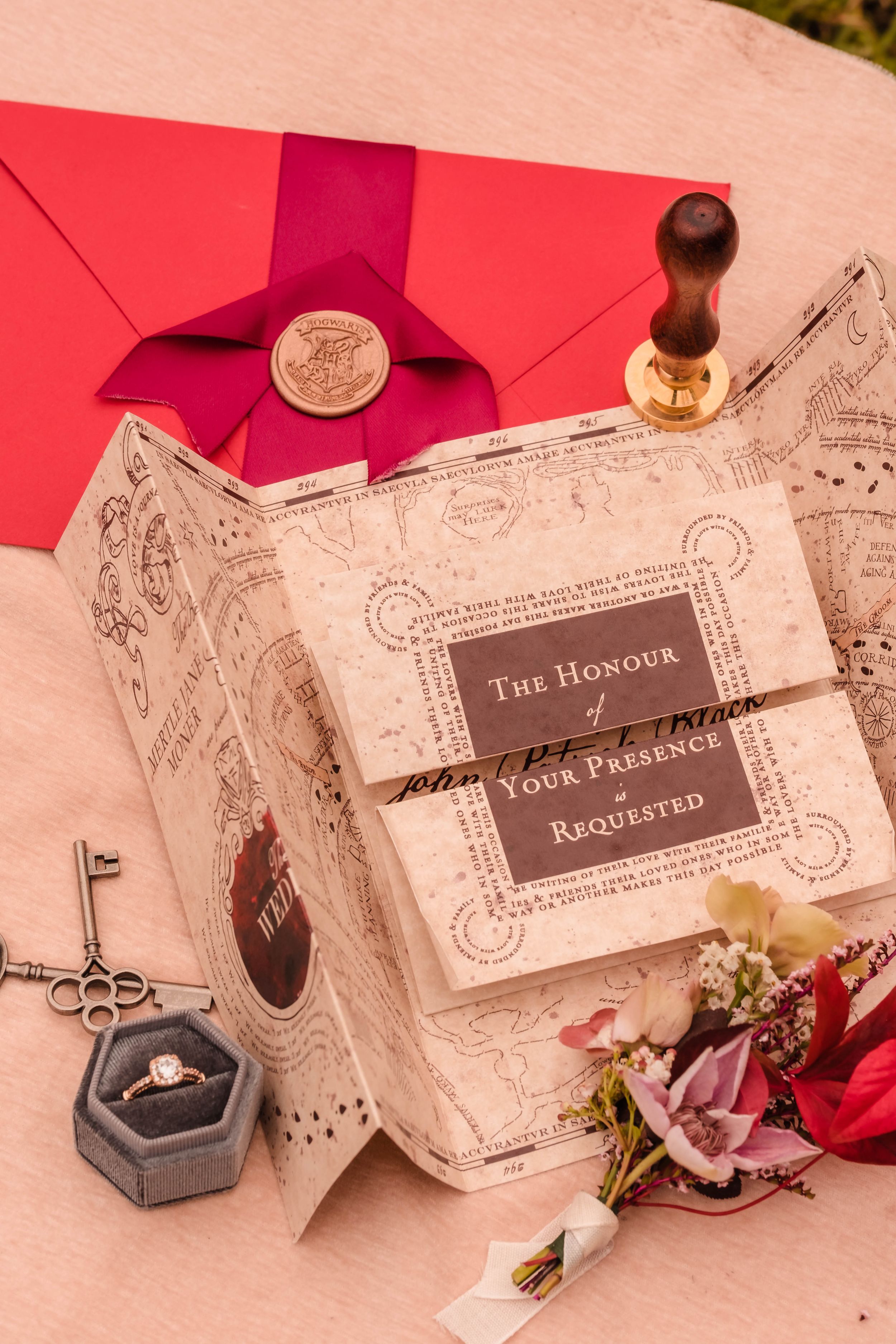 Harry potter style invitation cards and envelopes with decorative designs laid out on a pink surface. For a themed photoshoot.