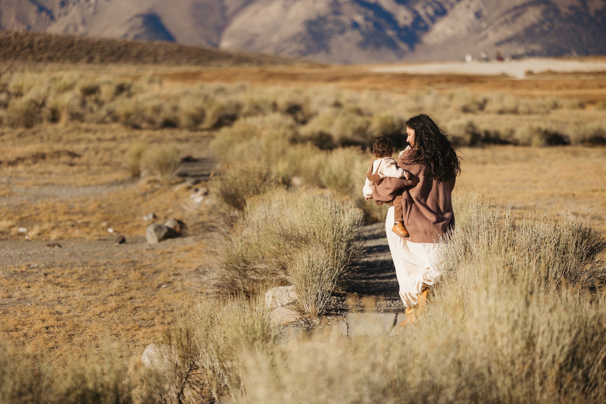 A person sits on rocky terrain overlooking a vast desert landscape during golden hour.