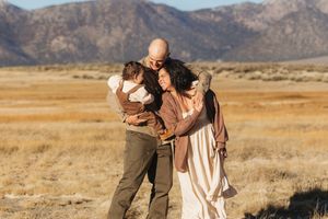 A family embraces together in a golden field with mountains in the background on a sunny day.