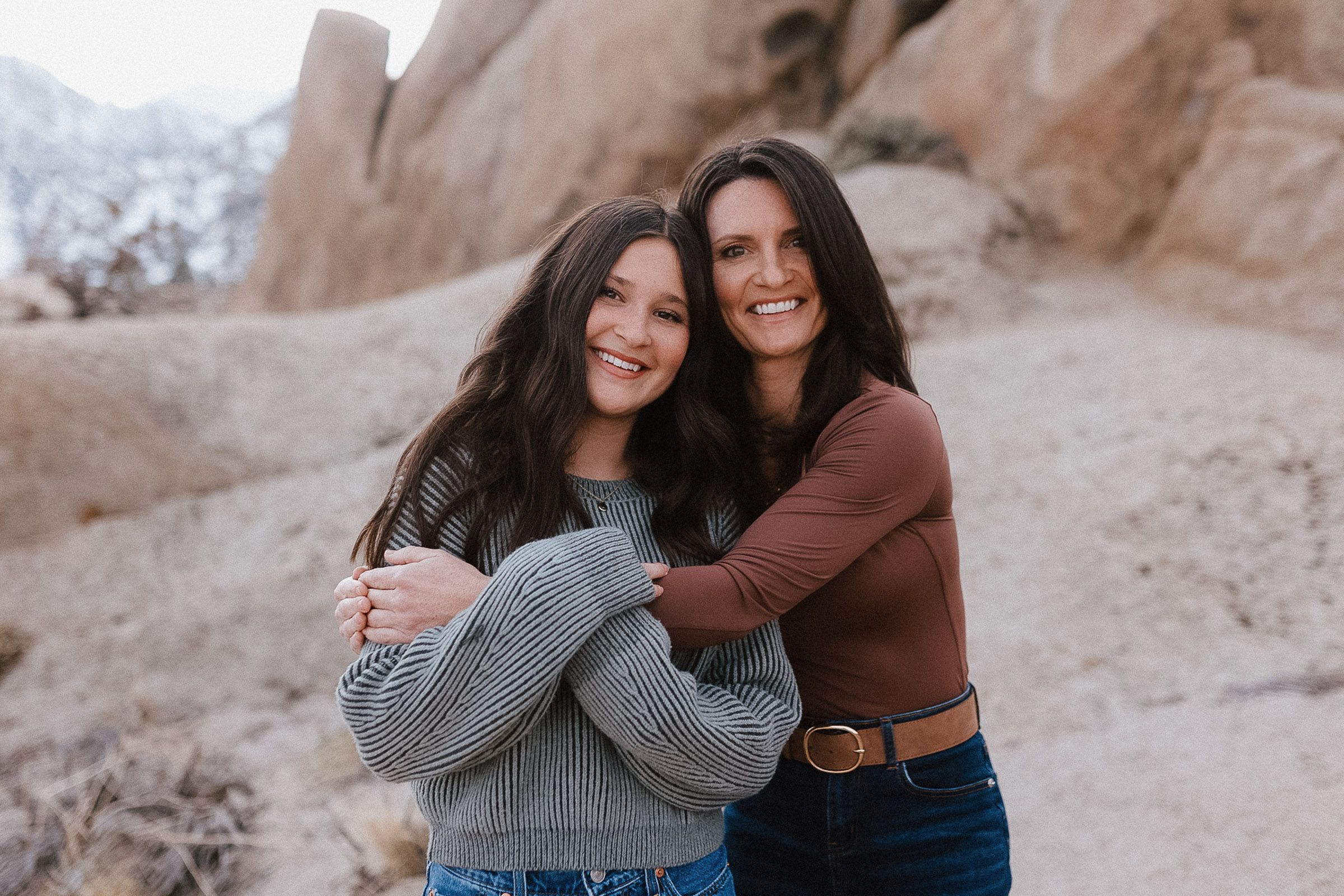 Two friends embrace and laugh together against a desert rock formation backdrop.