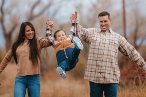 A playful family moment swinging a child in a field during autumn.