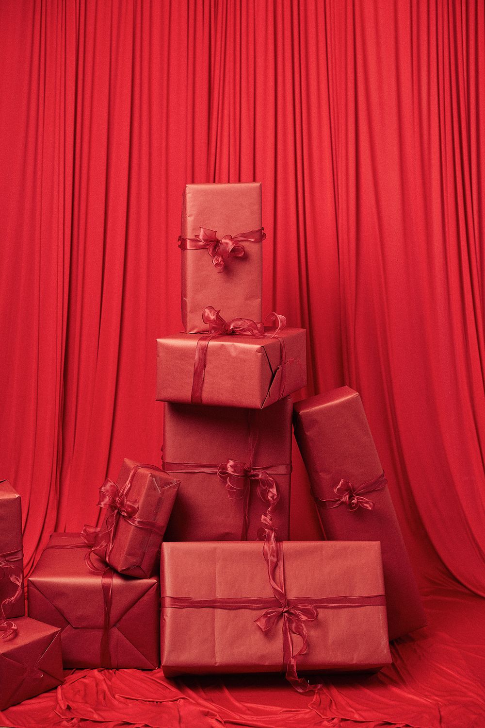 Stack of red wrapped presents arranged in pyramid shape against red curtain backdrop.