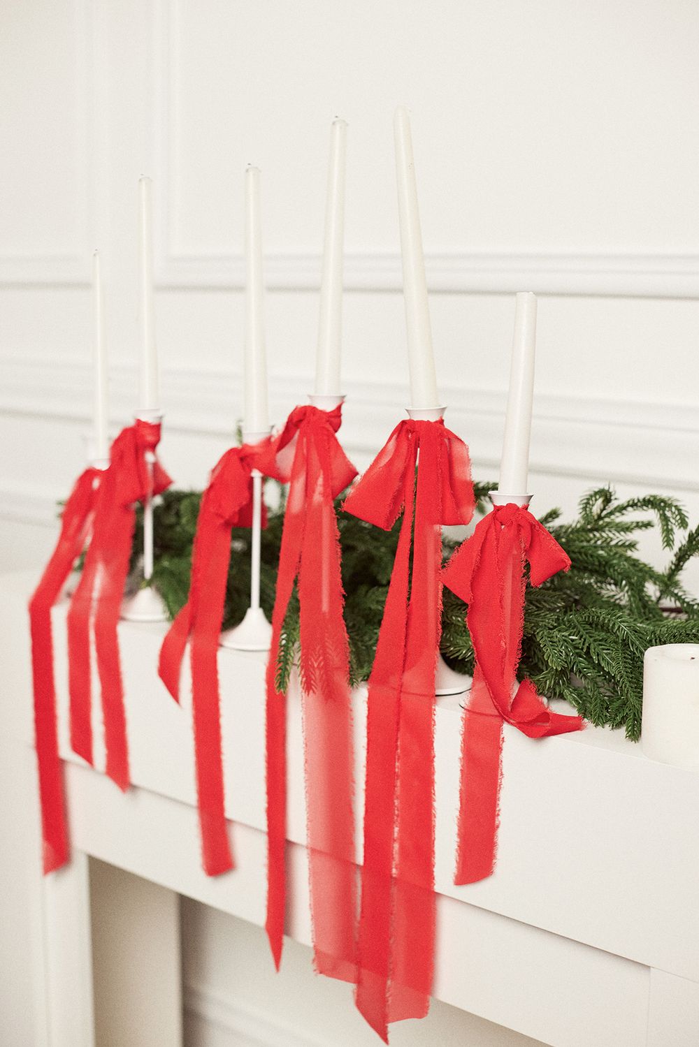 Red ribbons tied to evergreen garland against white wall in Christmas decor.