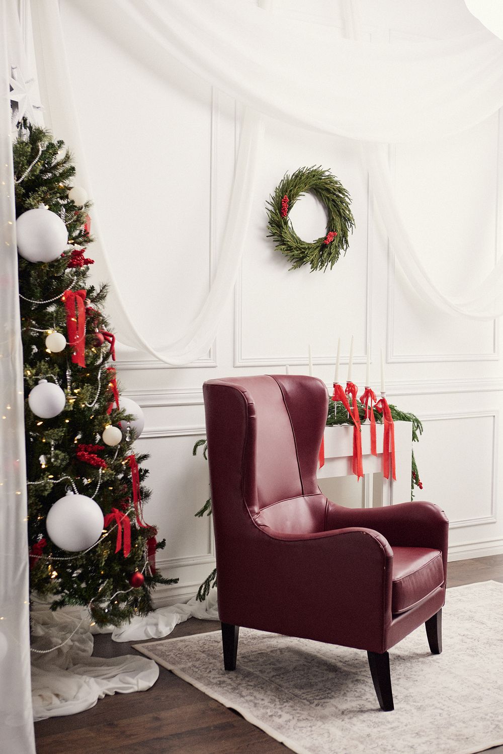 White Christmas room with burgundy chair, decorated tree and red ribbon garland.