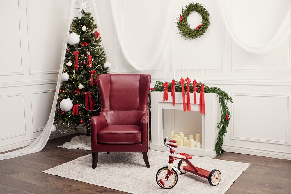 White Christmas room with burgundy armchair, decorated tree, and red tricycle.