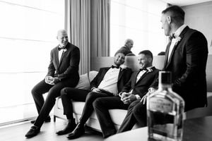 A black and white photo series captures someone in formalwear reclining on a modern sofa near large windows.