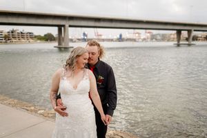 Romantic couple in wedding attire embracing by a waterfront on their special day.