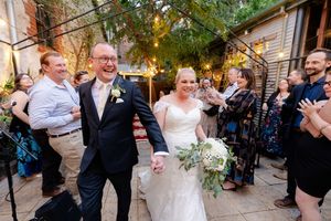 Wedding guests celebrate and laugh together during an outdoor garden reception beneath string lights and trees.