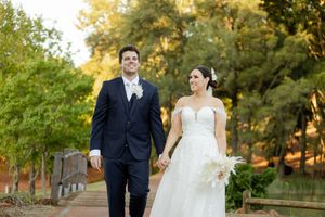 A couple in wedding attire strolls through a tree-lined path during golden hour at sunset.