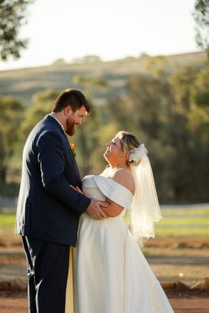 A romantic wedding couple shares an intimate moment at sunset in an outdoor setting.