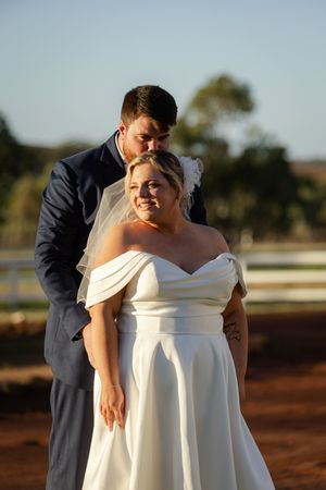 A bride in a white off-shoulder gown stands in golden sunlight during an outdoor photo session.