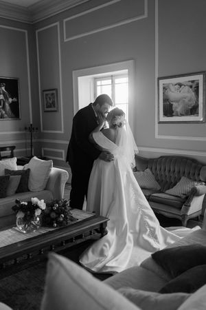 Black and white photo series showing a wedding dress being adjusted in an elegant room with antique furniture.