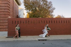 Two people lean against opposite sides of a red brick wall in a creative wedding photo composition at sunset.