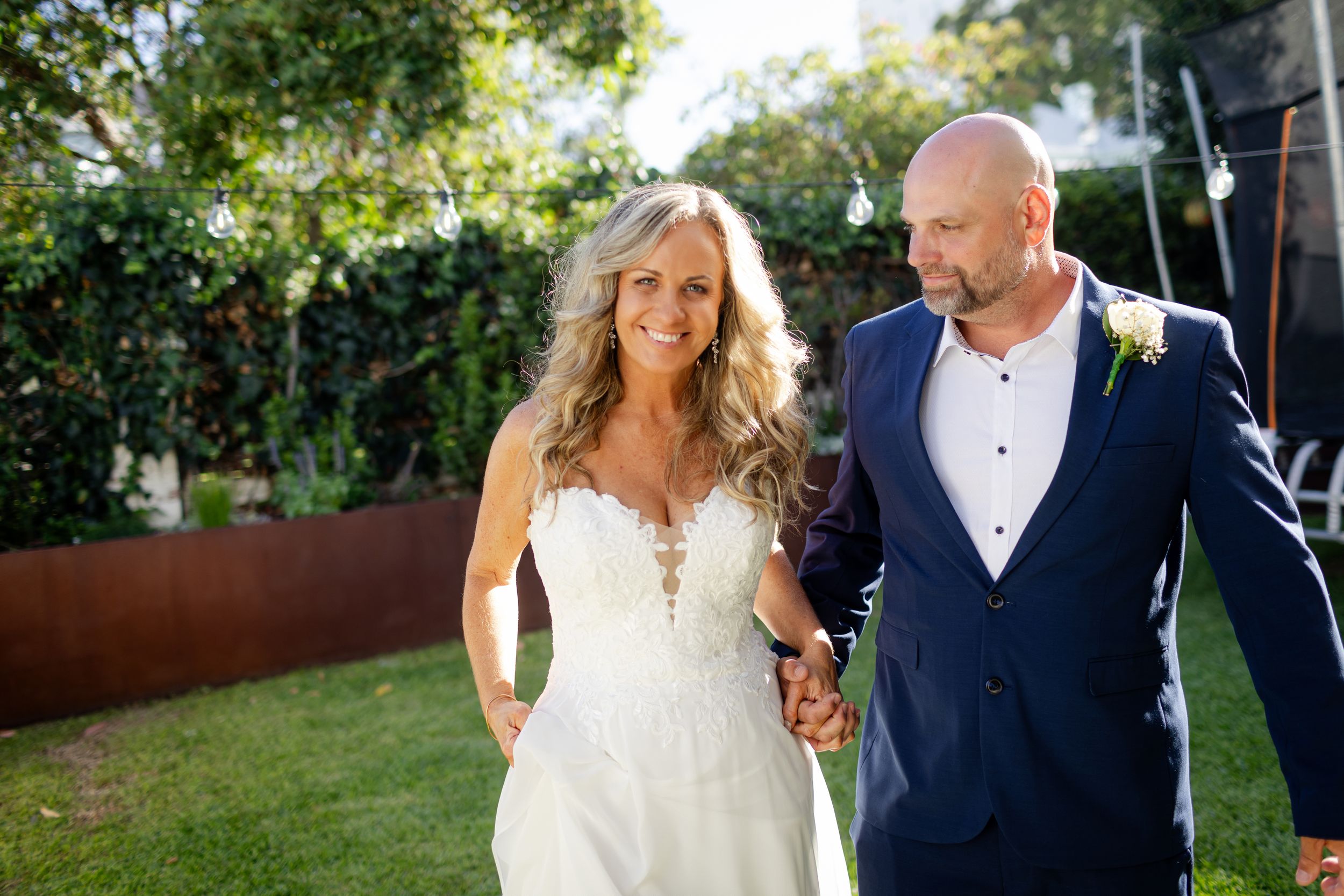 Newlyweds walk and laugh together in a lush garden setting during their wedding celebration.