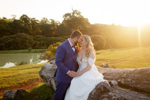 A couple shares a romantic sunset kiss on a grassy hillside during their wedding photoshoot.