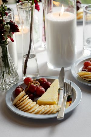White plates with crackers, cheese and grapes arranged beside glowing candles create an elegant appetizer spread.