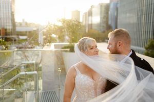 A couple shares a romantic moment on a rooftop terrace during golden hour with a cityscape backdrop.