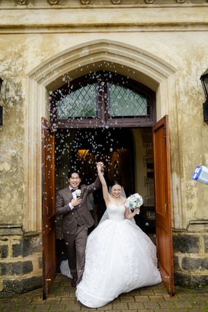 Newlyweds exit historic stone church doorway as guests shower them with confetti and rice in celebration.