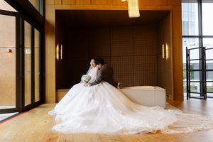 A flowing white wedding dress train extends gracefully across a modern interior hallway with wood floors and glass walls.