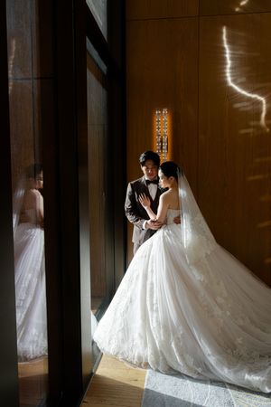 A bride in a flowing white ballgown wedding dress stands in dramatic silhouette against a window in an elegant venue.