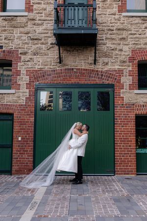 A romantic wedding couple shares a tender moment in front of green doors and stone walls at the Distillery District.
