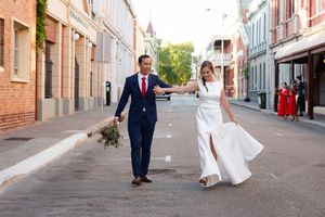 A couple in wedding attire walks together down a charming brick street lined with historic buildings.