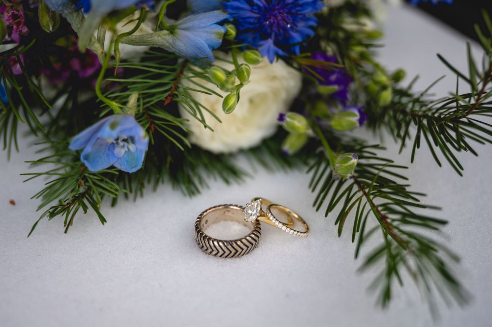A close-up view of blue and white flowers with evergreen sprigs arranged with delicate rings and jewelry pieces.