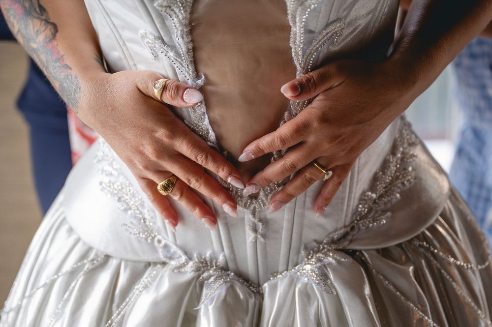 Close-up view of hands adjusting a white corset-style wedding dress with delicate lacing details.