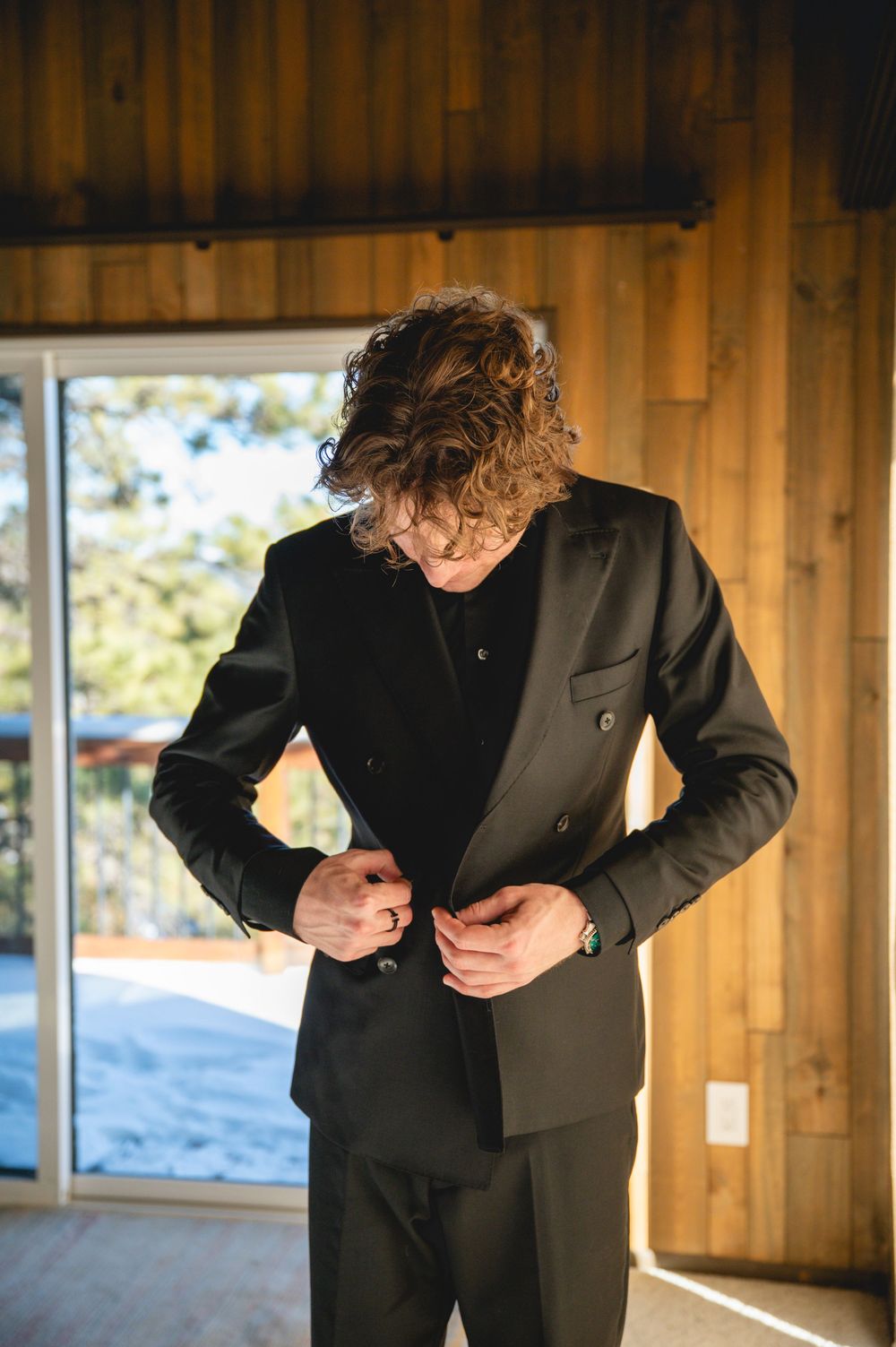 Person in black suit jacket bends forward in sequence of motion across wooden room with large windows.