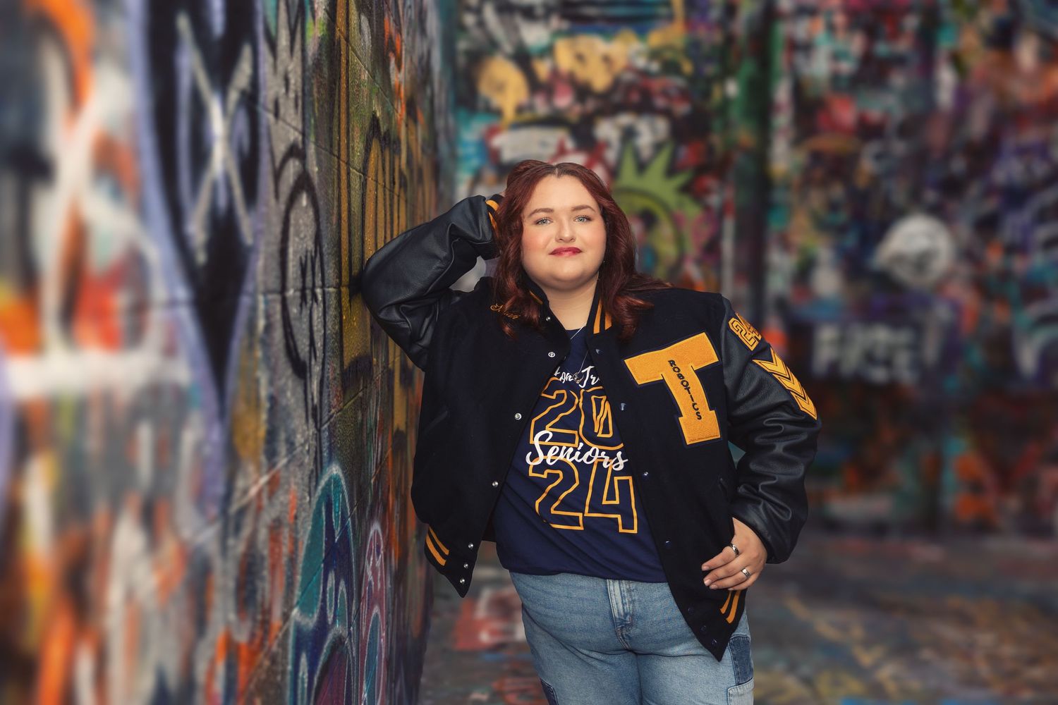 Person in black jacket and jeans poses against vibrant graffiti wall in urban setting.