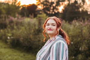 A person in a striped shirt stands in a garden at sunset with warm golden light filtering through trees.