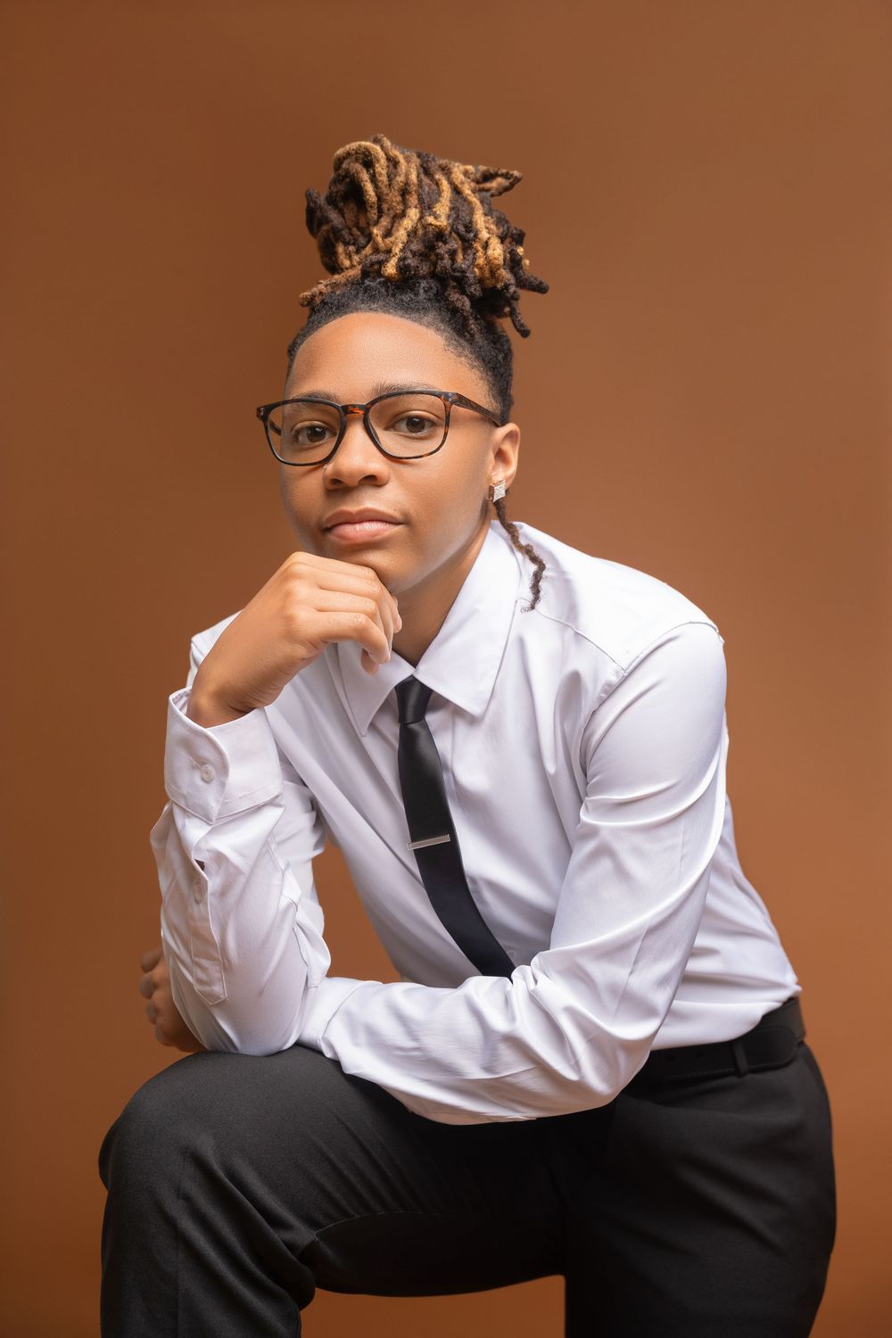 Shank Henry Media professional portrait against brown background showing person in white dress shirt, black tie and glasses with styled hair