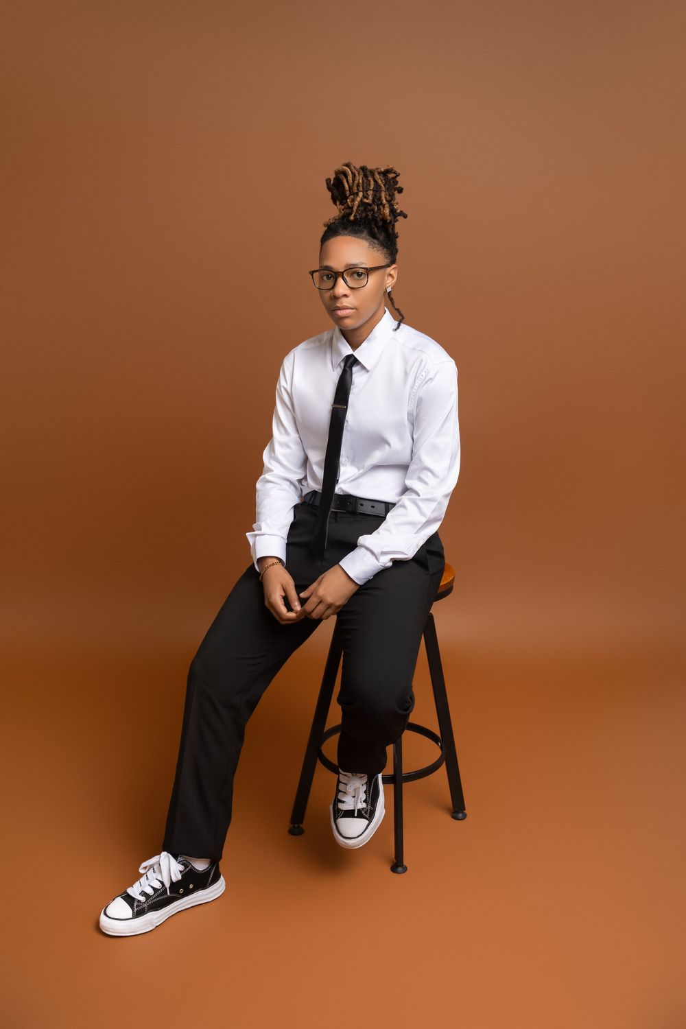 Person in business casual attire sits on black chair against brown backdrop in four different poses.