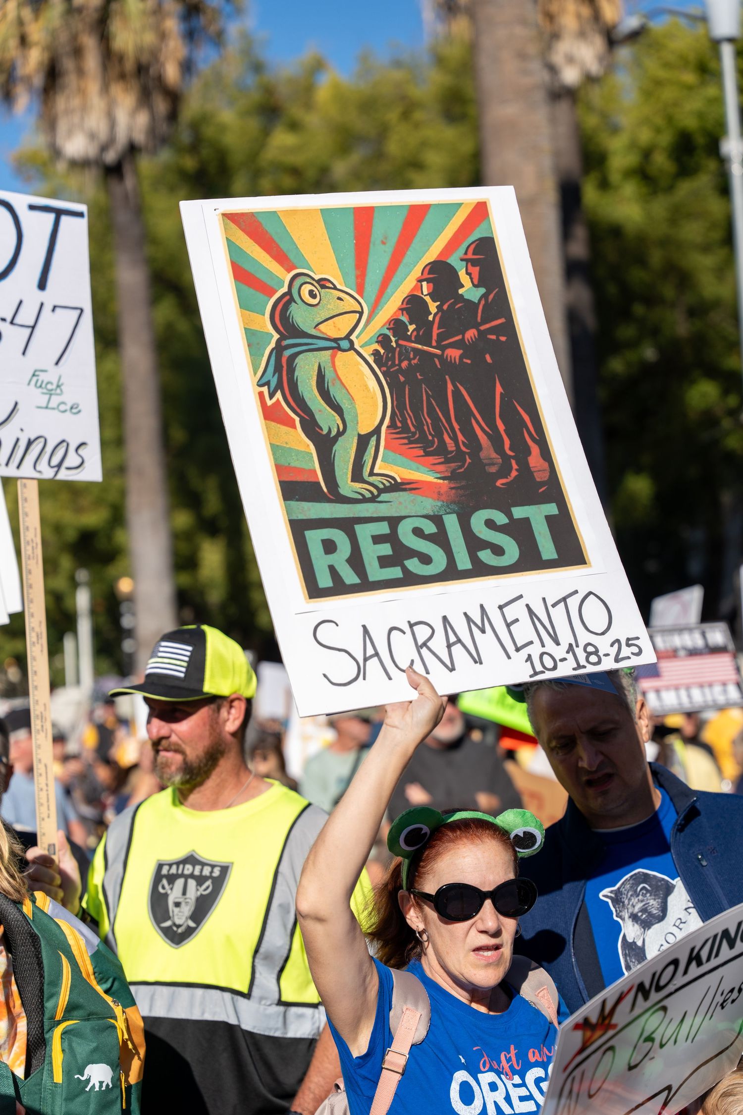 Protesters hold colorful signs with resistance messages at an outdoor demonstration in Sacramento.