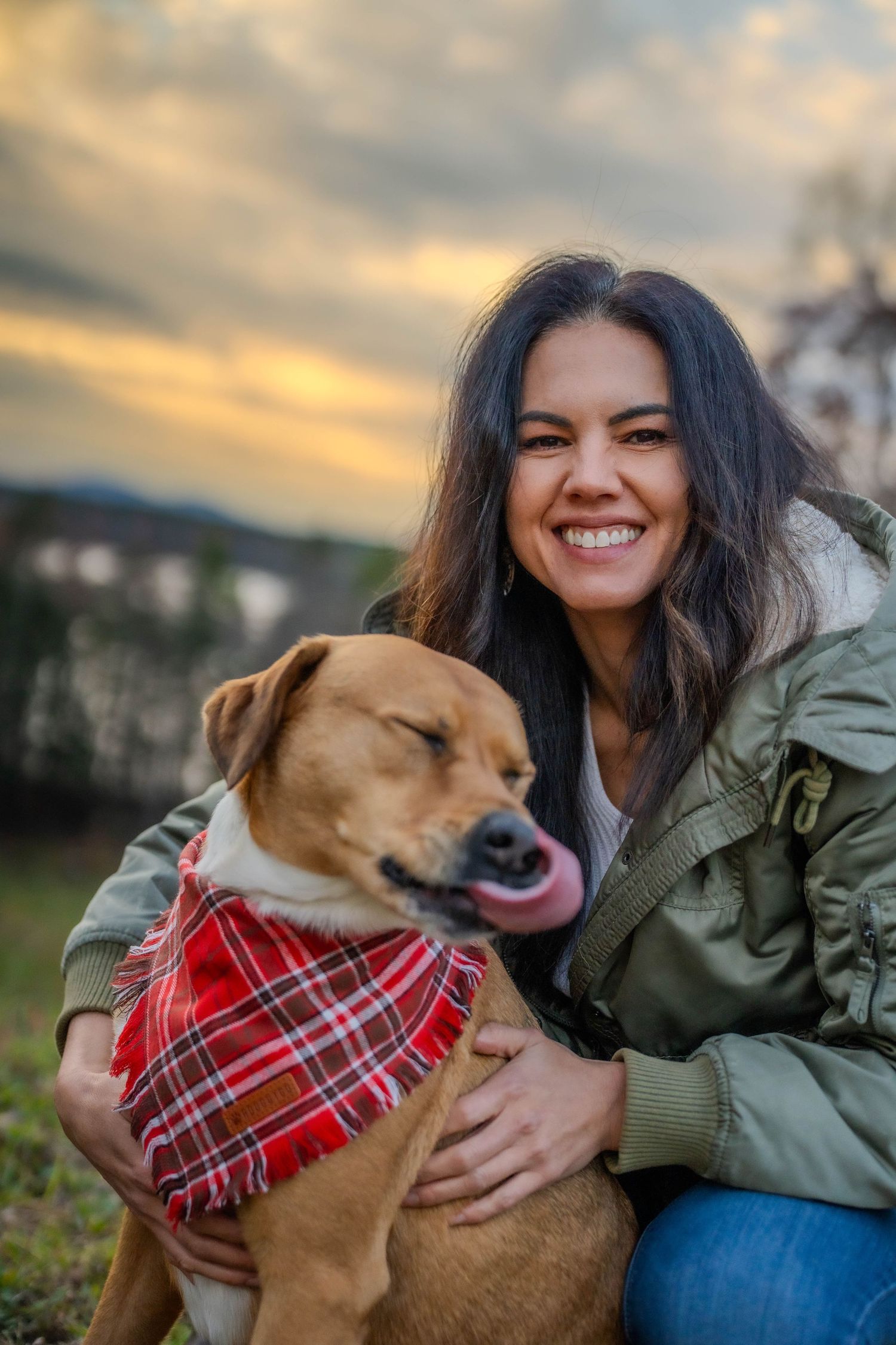 Person and dog with red plaid bandana enjoying outdoor sunset moment.