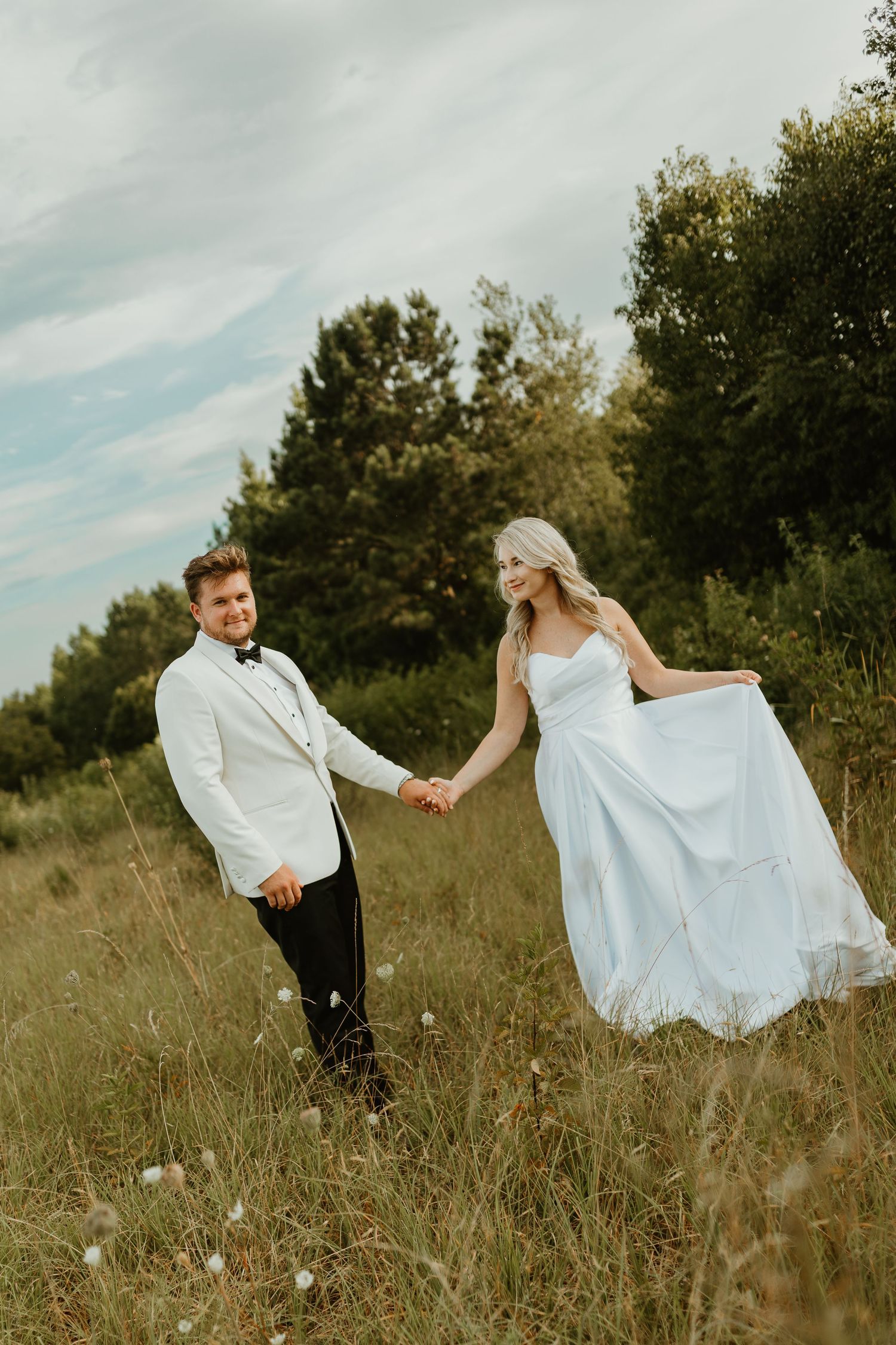 A couple in wedding attire dances playfully through a rustic field on their special day.