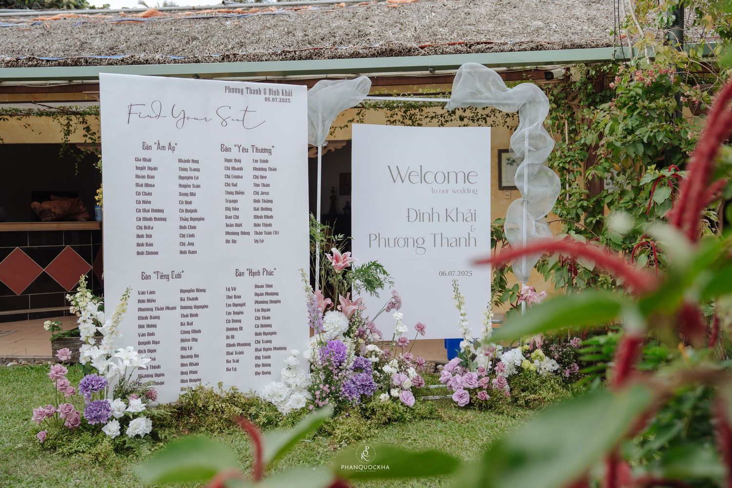 Wedding welcome sign and seating chart displayed on white boards surrounded by garden flowers.