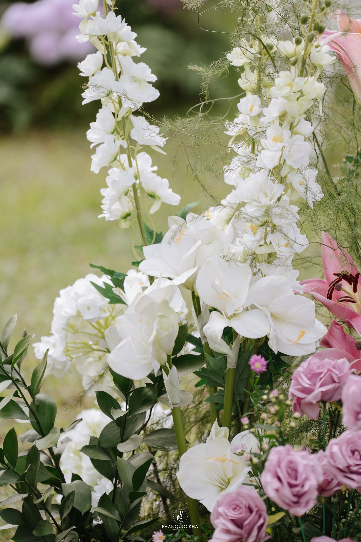 White delphiniums and pink roses in a lush garden floral arrangement for a romantic outdoor wedding.