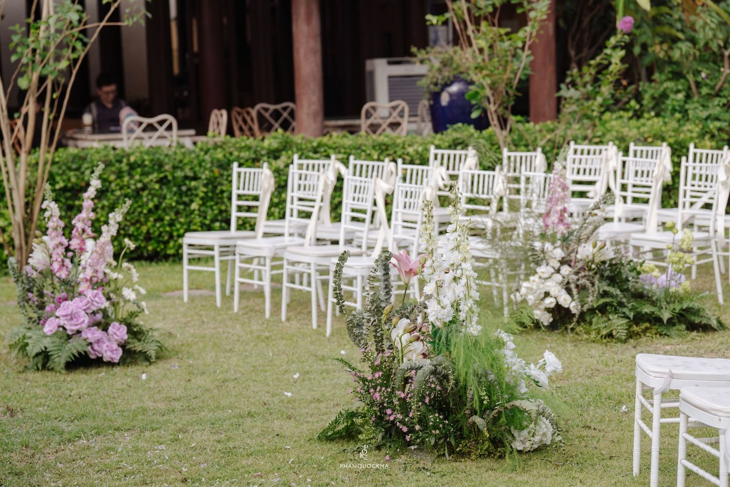 White Chiavari chairs and pink floral arrangements lining the aisle of an outdoor garden wedding ceremony.