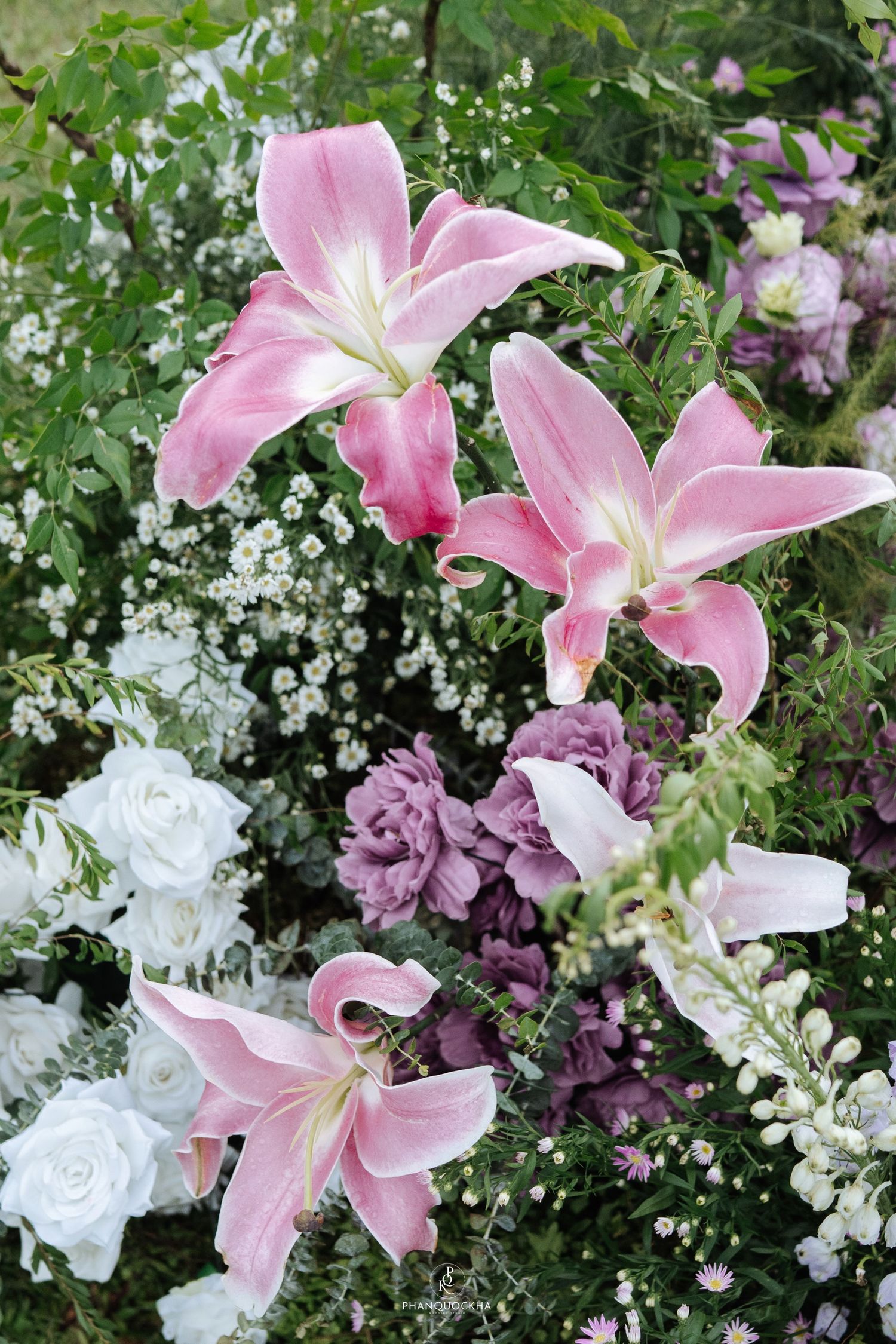 Close-up of beautiful pink lily flowers with white roses and purple blooms in a lush wedding floral arrangement.
