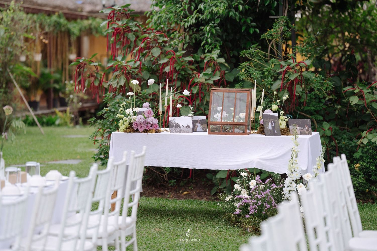 Outdoor garden wedding ceremony setup with white chiavari chairs and decorated signing table surrounded by lush greenery.