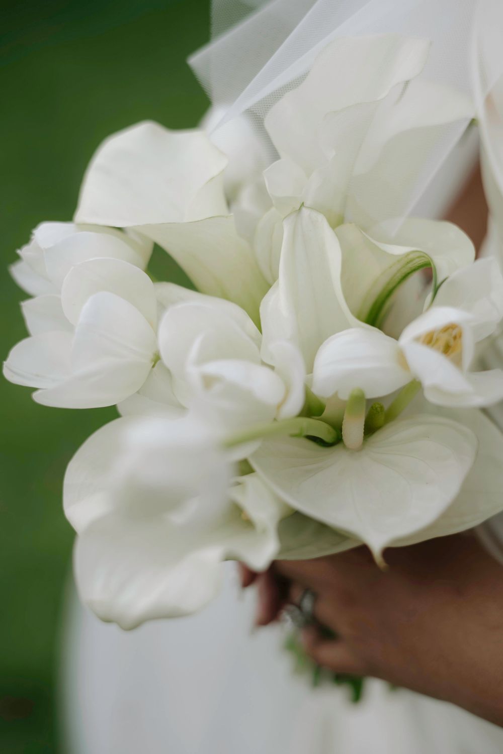 Close-up of elegant bridal bouquet featuring white orchids and calla lilies held by bride in white dress.