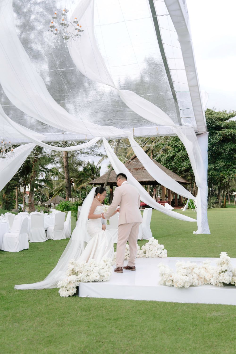 Bride and groom share intimate moment under flowing white draped canopy at outdoor garden wedding ceremony.