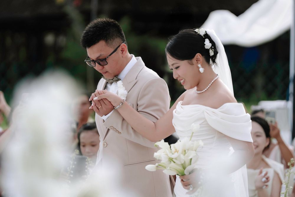 Groom places ring on bride's finger during outdoor wedding ceremony as guests watch.