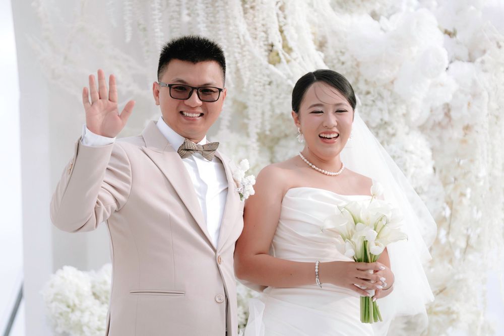 Smiling bride and groom waving at their elegant all-white wedding ceremony.