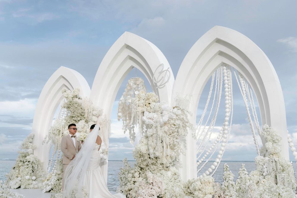 Couple embracing under white floral arches at stunning oceanfront wedding venue.