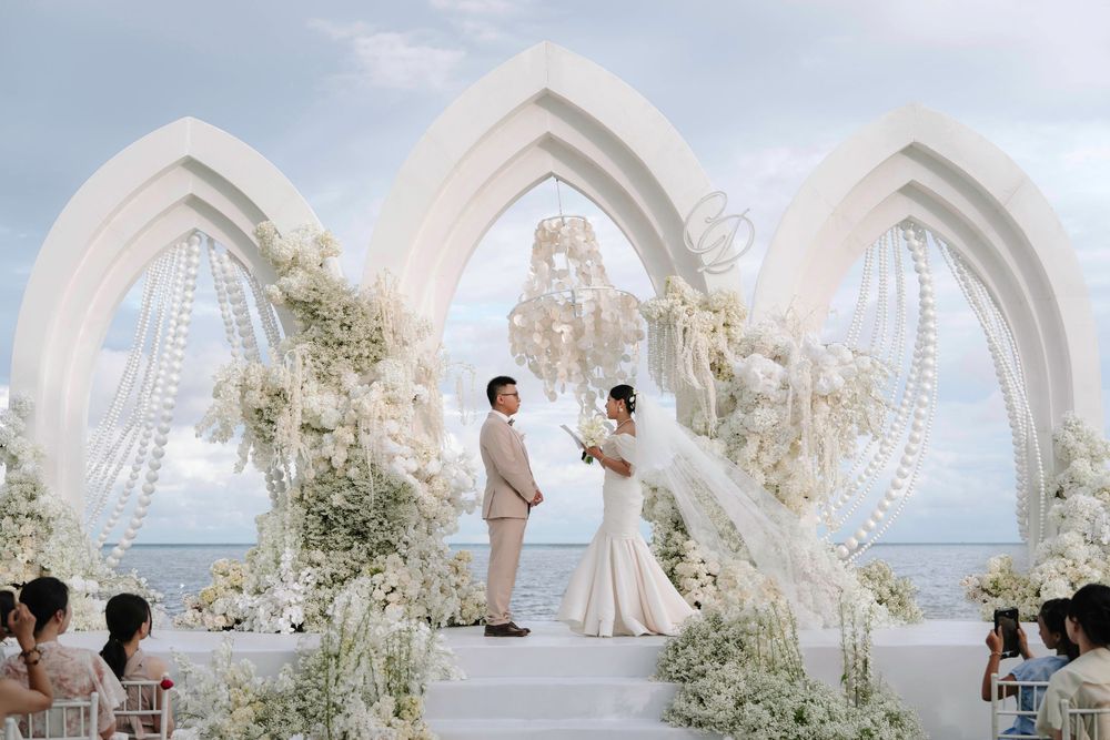 Bride and groom exchanging vows under ornate white arches at seaside wedding.