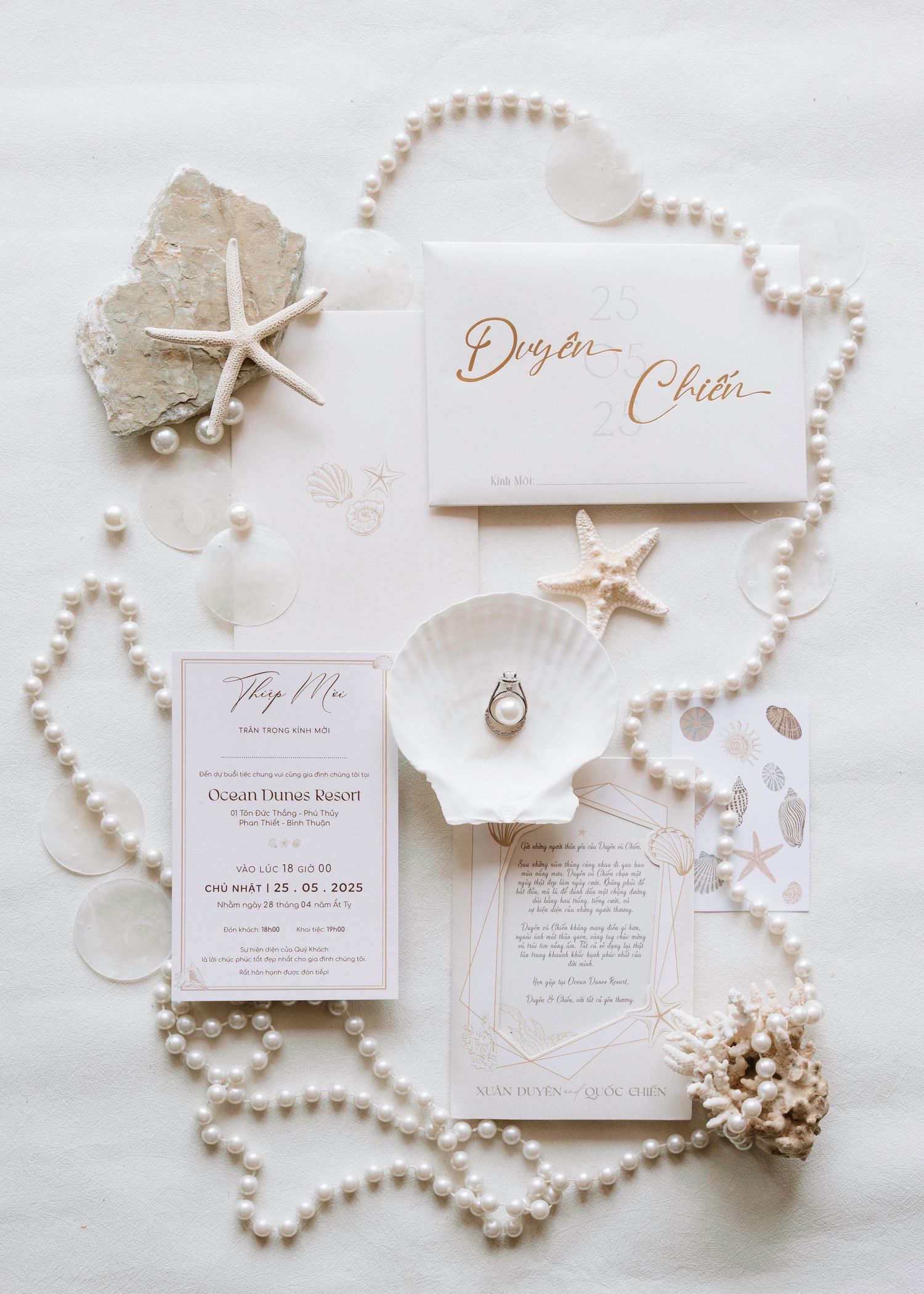 Coastal wedding stationery flatlay with pearls, starfish, seashells, and rose gold calligraphy invitations.