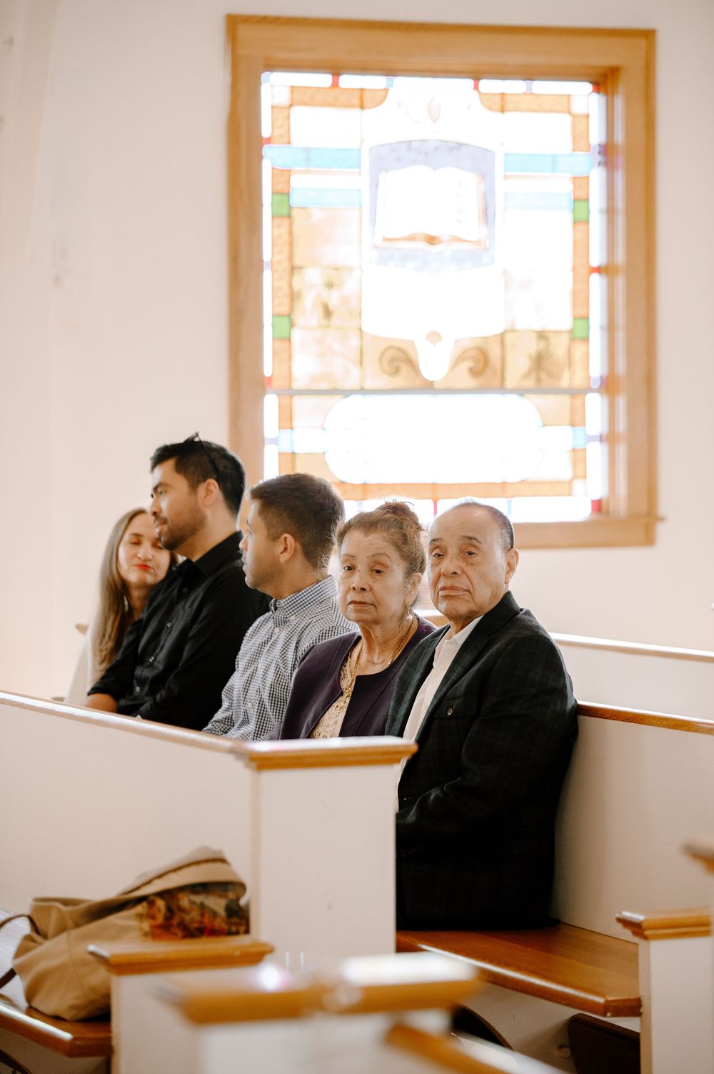 Several people seated together in wooden church pews during a ceremony.