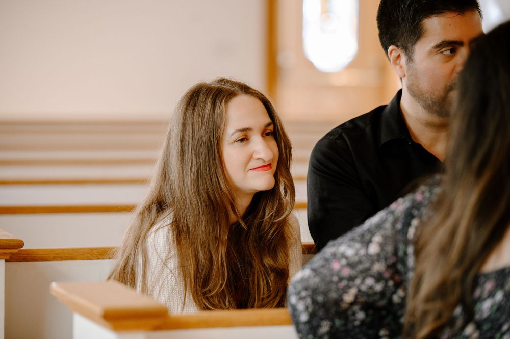 People seated in bright white church pews with natural light streaming through windows.